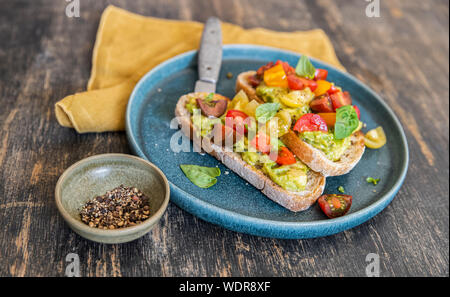 Photo appétissante de deux tranches de pain au levain avec de l'avocat, des tomates cerises rouges et jaunes et de basilic dégoulinant de olil olive sur une plaque bleue Banque D'Images