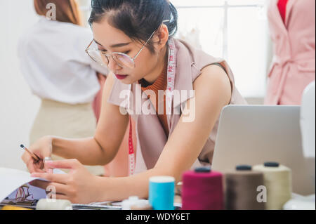 Jolie Asian female fashion designer working in clothing shop avec le client. Fashionista élégant femme créant de nouvelles collections design en tissu Banque D'Images