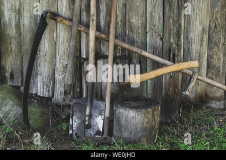 Très vieux, rouillé et sale de travail Outils de jardin rural (houe, râteau, bêche, faux, hache, pitchfork) près de la grange de boiseries en campagne Banque D'Images