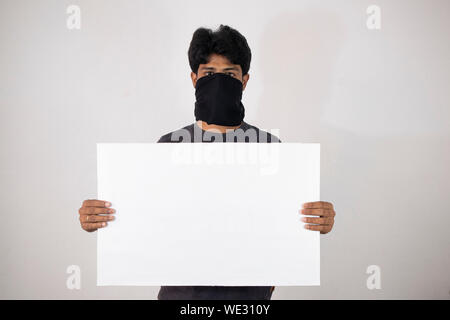 Concept de protestation montrant avec homme debout en couvrant le visage avec le tissu noir et la tenue de bannière, un placard vide sur isloated arrière-plan. Banque D'Images