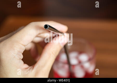 Hand holding metal paille dans un verre de boisson sucrée rouge Banque D'Images