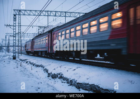 Train à grande vitesse dans la neige. Les lumières sont allumées à l'intérieur du chariot. Les passagers faisant leur chemin du travail à bord d'un train de banlieue dans la soirée. Banque D'Images