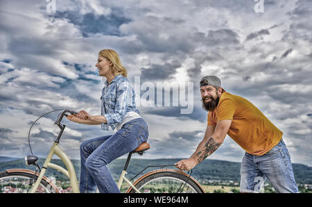 Des promenades en vélo femme fond de ciel. Pousser et la promotion. Impulsion à se déplacer. Homme pousse fille faire du vélo. Aide à croire en vous-même. Impulsion L'impression de commencer à bouger. Vélo fille tandis que l'homme la soutenir. Banque D'Images