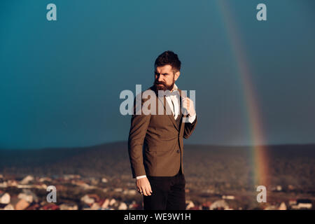 Homme avec barbe et moustache et paysage avec arc-en-ciel sur l'arrière-plan. Hipster avec élégance en face de ciel dramatique avec arc-en-ciel. La masculinité Banque D'Images