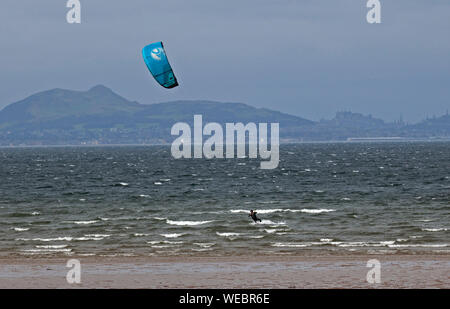 Longniddry Bents, East Lothian, Scotland, UK. Août 30, 2019. Un seul Kite Surfer out Kiteboarding brave la Firth of Forth saccadée et des rafales de vent à Longniddry où conditions morne terne a fait place à un éclaircissement du ciel par MIDI, avec le Château d'Édimbourg et le siège d'Arthur en arrière-plan. Vent estimée : 42 km/h SW. Rafales de vent : 63 km/h. Banque D'Images