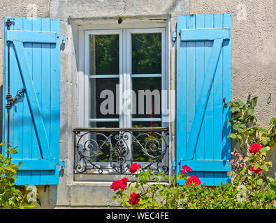 Le Sunny View en face d'une fenêtre avec volets d'une vieille maison de ferme, avec un buisson de fleurs roses et de fleurs qui y poussent de nombreux Banque D'Images