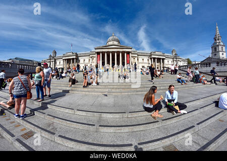 Londres, Angleterre, Royaume-Uni. Trafalgar Square - les gens assis sur les marches en face de la Galerie Nationale Banque D'Images