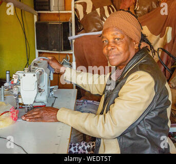 Windhoek, Afrique du Sud - Juillet 6, 2018 : un tailleur coud des vêtements pour la vente dans une minuscule boutique en Namibie Banque D'Images