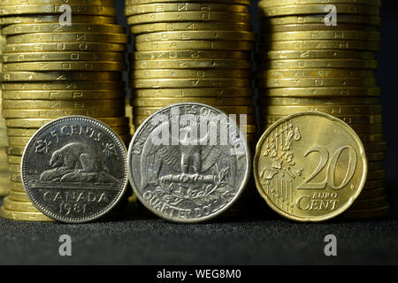 Trimestre pièce de un dollar, cinq cents Canadiens et 20 euro cent coin placé sur les bords en face de Piles of Coins Banque D'Images