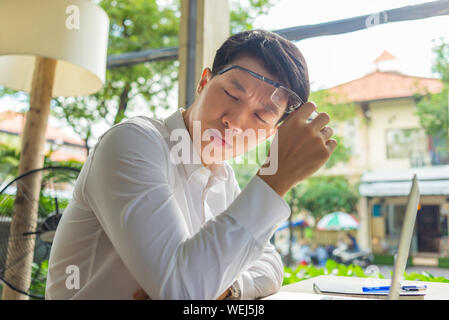 Fatigué businessman taking off ses lunettes tout en travaillant sur l'ordinateur portable Banque D'Images