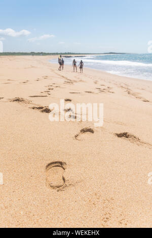 Footprints le long de la côte de sable, un groupe de quatre personnes sont à la plage, l'océan vient d'une seule vague, dans l'horizon il y a quelques Banque D'Images