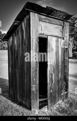 Vieux, out-house, et assez ou, avec porte ouverte avec toit rouillé sur une colline avec des arbres sur le terrain dans le sud-est des États-Unis , en noir et blanc Banque D'Images