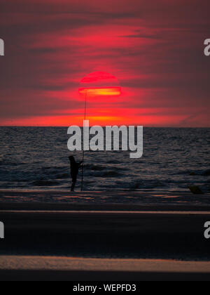 Silhouette d'un pêcheur sur la plage en face de la grande coucher de soleil Banque D'Images