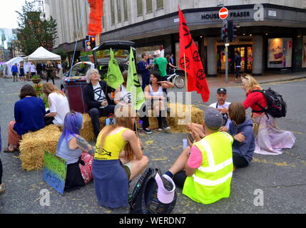 Un groupe est assis sur des bottes de paille à l'extérieur Kendals magasin comme rébellion du nord protestataires, partie du mouvement global Extinction Rébellion, bloqué de Deansgate et ses rues transversales dans le centre de Manchester, Royaume-Uni, le 30 août, 2019 au début d'une manifestation de quatre jours. Les manifestants demandent que le gouvernement dit la vérité à propos de l'urgence climatique, prend des mesures maintenant, et est dirigée par une assemblée de citoyens sur le changement climatique. Banque D'Images