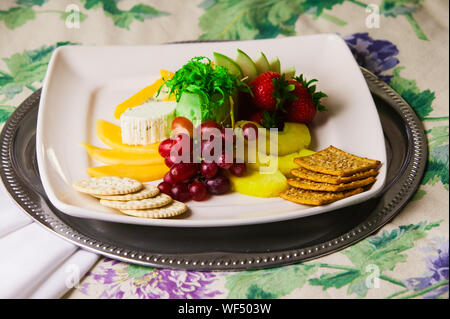 Plaque blanche rempli de raisins, fraises, ananas, fromage et craquelins. Banque D'Images