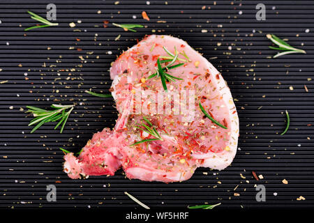 La viande crue sur fond sombre. Steak de porc aux herbes et épices Banque D'Images