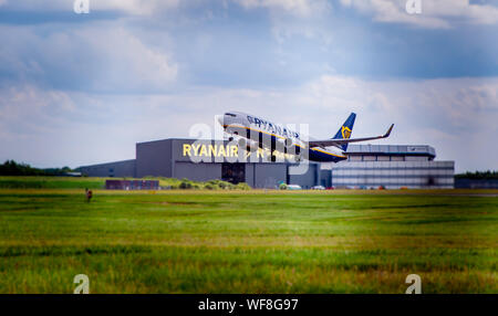 L''aéroport de Stansted, ESSEX / UK - circa 2019, juillet : Ryanair Boeing 737 décolle avec Ryanair visibles en arrière-plan de hangar Banque D'Images