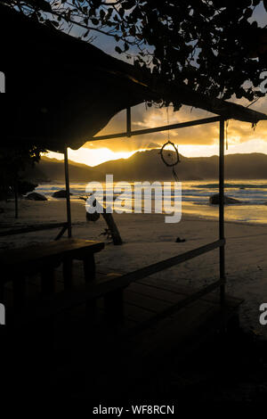 Vue d'un magnifique coucher de soleil à travers les montagnes et par la plage avec la lumière du soleil se reflétant dans la mer Banque D'Images