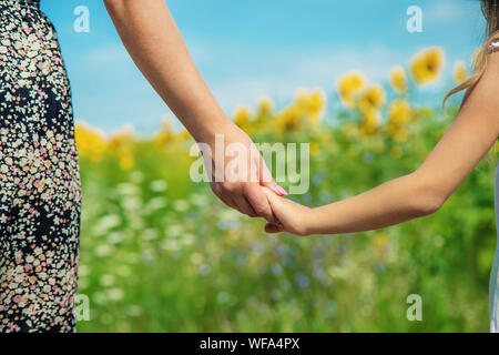 Mère et fille vont main dans la main dans un champ de tournesols. Focus sélectif. nature. Banque D'Images