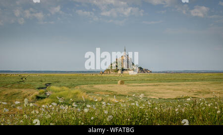 Belle vue panoramique sur le Mont Saint-Michel célèbre île de marée avec de l'eau d'un bleu profond et clair à reflets lumière du soir au coucher du soleil d'or à l'al. Banque D'Images