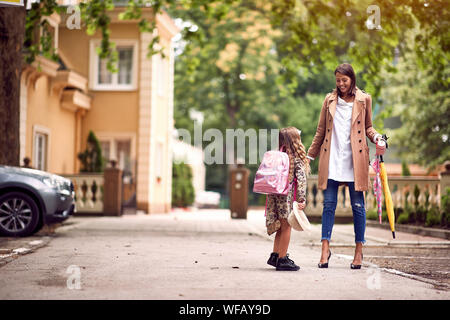 Cute little girl avec des sacs à dos pour aller à l'école avec sa mère souriante Banque D'Images