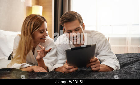 Portrait de couple allongé sur le lit et de regarder l'écran du PC tablette. Voyageant ensemble concept. Plan horizontal. Vue avant Banque D'Images