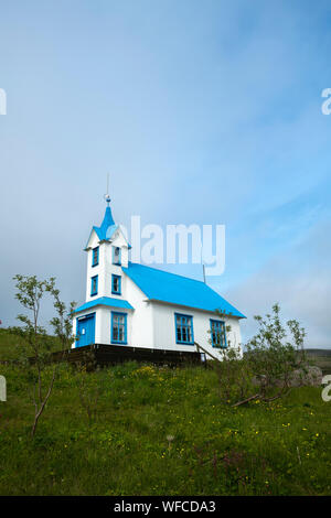 Bleu et blanc Stödvarfjördur église convertie en maison d'hôtes sur une petite colline herbeuse vert avec soft coulds sur une journée ensoleillée en Islande Banque D'Images