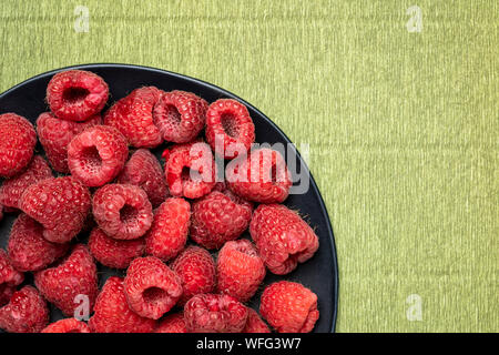 Les framboises rouges frais sur une plaque noire contre papier crêpe vert par un arrière-plan copy space Banque D'Images