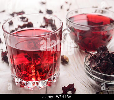 Vue rapprochée à deux tasses de thé avec de la glace sèche et pétales d'hibiscus sur fond de table en bois blanc Banque D'Images