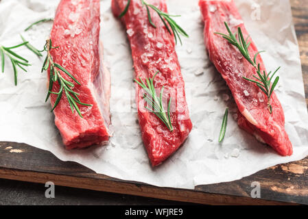 New York Strip Steak avec le sel et le romarin sur fond noir, vue du dessus, Close up. La bande de b oe uf cru non cuit les steaks. Banque D'Images