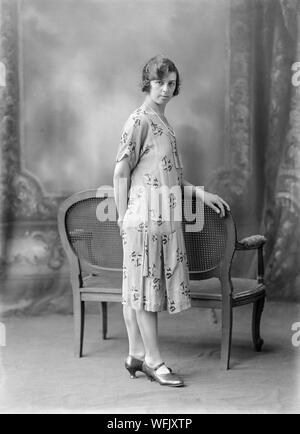 Au début du vingtième siècle vintage noir et blanc photographie, prise dans un studio photographique, montrant une jeune femme, dans une robe typique de la mode de la période, posant pour l'appareil photo tandis que l'article. Banque D'Images