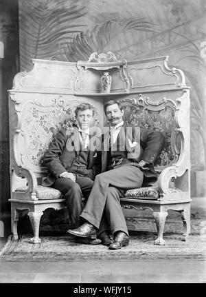 Un vintage style victorien ou au début de l'Edwardian Photographie noir et blanc montrant deux hommes, assis, posant dans un studio photographique. Un homme a une très grande moustache. La pose est très formel, mais également tout à fait détendue. Banque D'Images