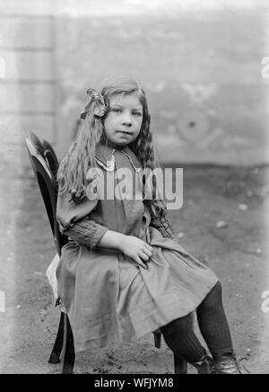 Un vintage style victorien ou au début de l'Edwardian Photographie noir et blanc montrant une jeune fille aux cheveux longs, dans une posture assise dans un studio photographique. Banque D'Images