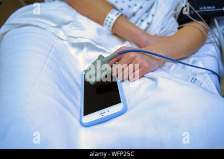 Patient au repos à l'hôpital avec un oxymètre attaché à part le fait de prendre une pause à partir de l'utilisation du smartphone. Banque D'Images