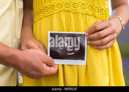 Young couple holding pregnat noir et blanc image échographique de leur bébé dans les champs de lavande avec des vêtements jaunes Banque D'Images