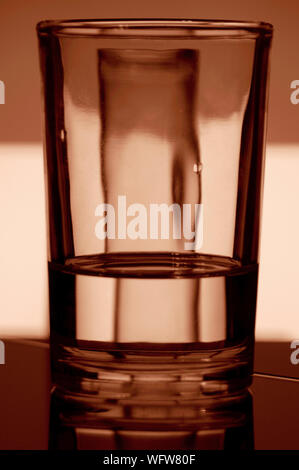 Un verre d'eau réfracte la lumière d'un fond coloré Banque D'Images