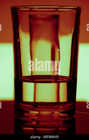 Un verre d'eau réfracte la lumière d'un fond coloré Banque D'Images