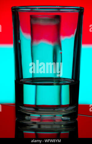 Un verre d'eau réfracte la lumière d'un fond coloré Banque D'Images