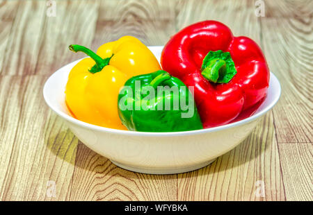 Rouge, vert et jaune les poivrons (Capsicum) dans un bol blanc sur une table en bois. Banque D'Images