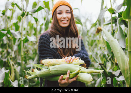 De beaux cheveux longs sans souci dans la fille asiatique et chapeau jaune chandail tricoté holding épis de maïs à l'automne. Sensibilité à la notion de la nature Banque D'Images