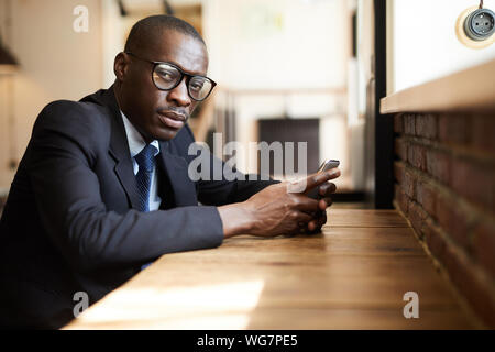 Portrait de l'homme afro-américain graves portant des lunettes à la caméra à l'aide de tout smartphone dans cafe, copy space Banque D'Images