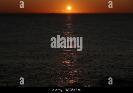 Un cargo à l'horizon comme le soleil se lève à Seahouses sur le Nord de la côte de Northumberland. Banque D'Images