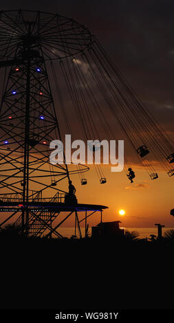 Carrousel oscillante chaîne rond-point ride au coucher du soleil. Le divertissement sur la plage, les silhouettes des palmiers sur fond de coucher de soleil sur la mer Banque D'Images