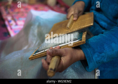 Femme avec des pinceaux la préparation d'une laine pour spining une chaîne en laine pour tapis marocain berbère. Banque D'Images