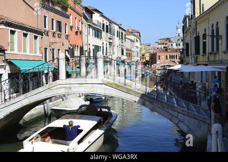 Bateau navigue entre une rangée sous un pont dans une rue de l'eau, un canal à Venise en Italie. Banque D'Images