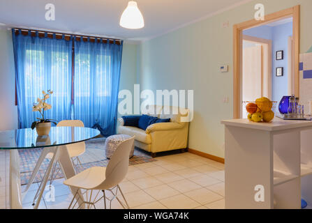 Salon élégant d'un petit appartement, avec une table en verre moderne et une partie de la kitchenette visible sur le droit Banque D'Images