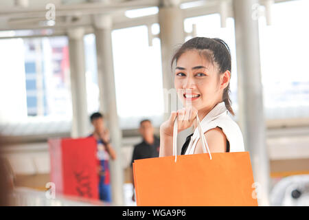Side View Portrait Of Smiling Young Woman Holding Shopping Bags In Covered Bridge