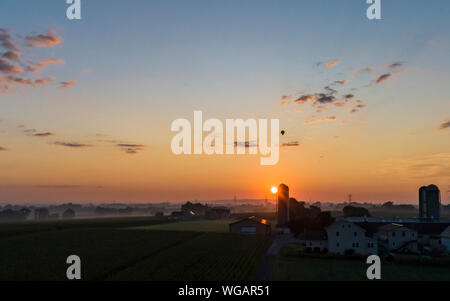 Une vue aérienne d'un lever de soleil au-dessus d'une ferme Amish avec bleu et rouge avec un ballon à air chaud flottant à un clair matin d'été Banque D'Images