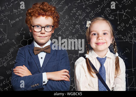 Cute school kids portrait. Petite fille et garçon school student sur fond noir avec des formules mathématiques et sciences Banque D'Images