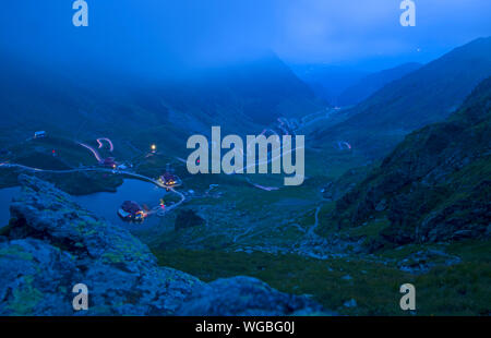 Lac de montagne en soirée et des feux de route sinueuse dans les montagnes de Fagaras, Roumanie Banque D'Images